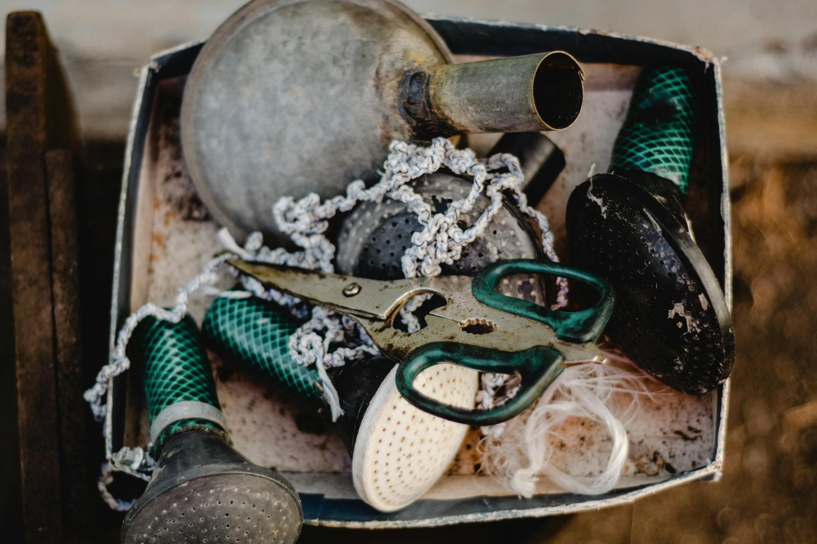 A collection of rustic gardening tools including scissors, watering can tips, and threads in a vintage box.