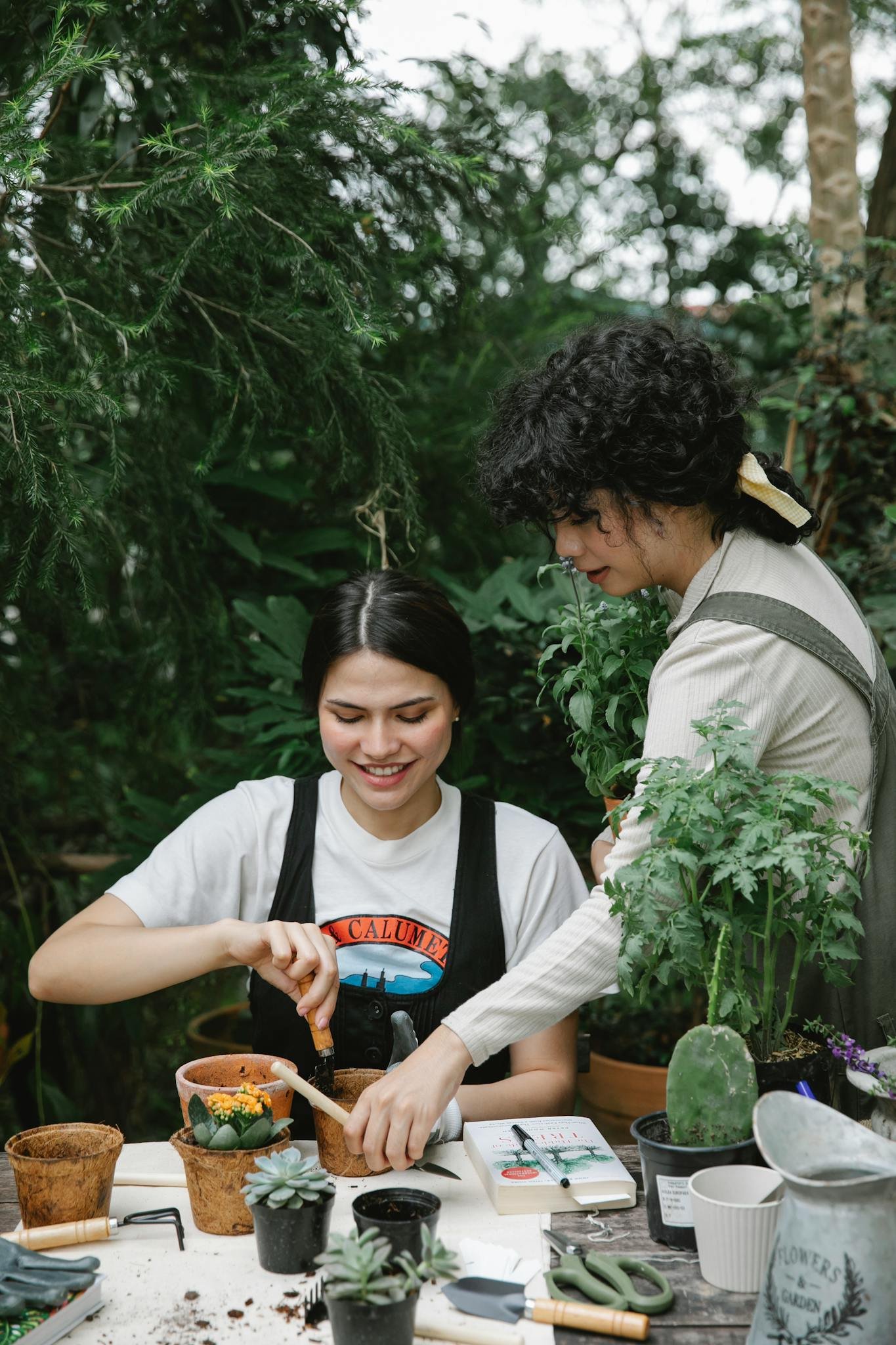 Positive female gardener with instrument planting seedling with colleague taking shovel from table